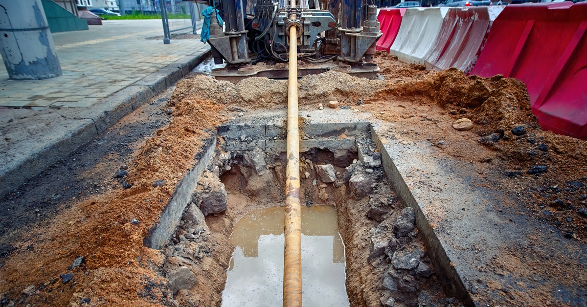 A horizontal directional drilling machine sits at the top of a trench at a construction site, laying underground pipes.