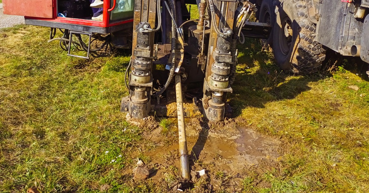 A directional drilling operation is underway, with an HDD machine on muddy terrain, a worker seated inside.
