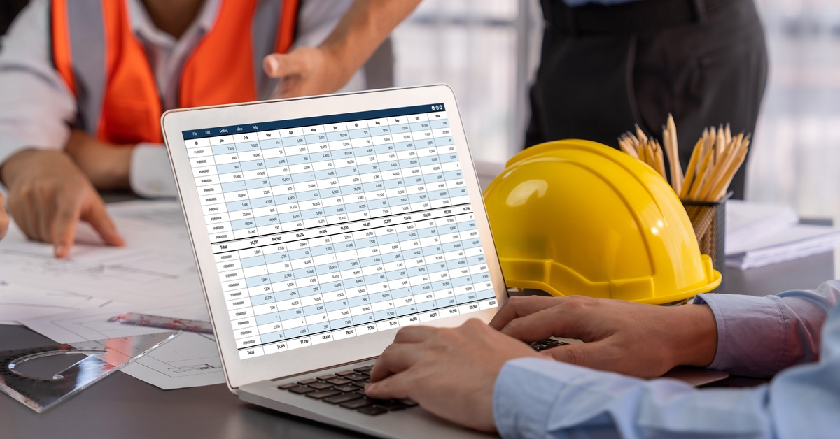 A laptop displaying a financial spreadsheet on the screen, surrounded by hands pointing at documents, with a yellow hard hat nearby.