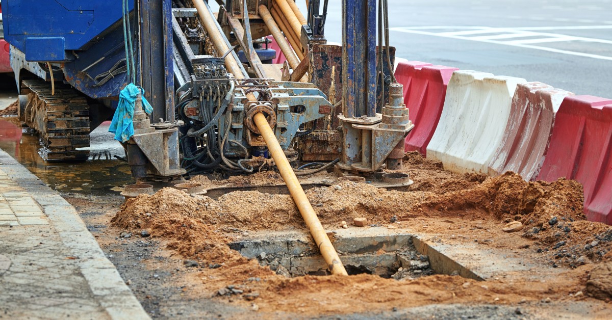 A horizontal directional drilling machine operates on a construction site, drilling into the ground near a trench.