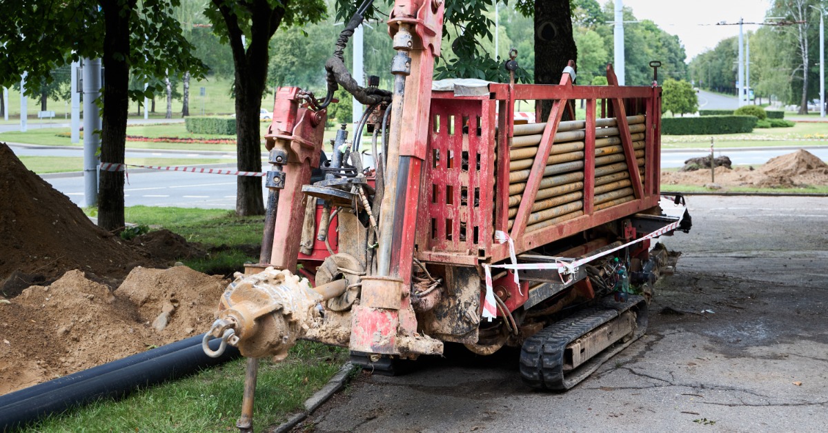 A directional drilling machine stands on paved ground with attached pipe and drilling components visible at the front.