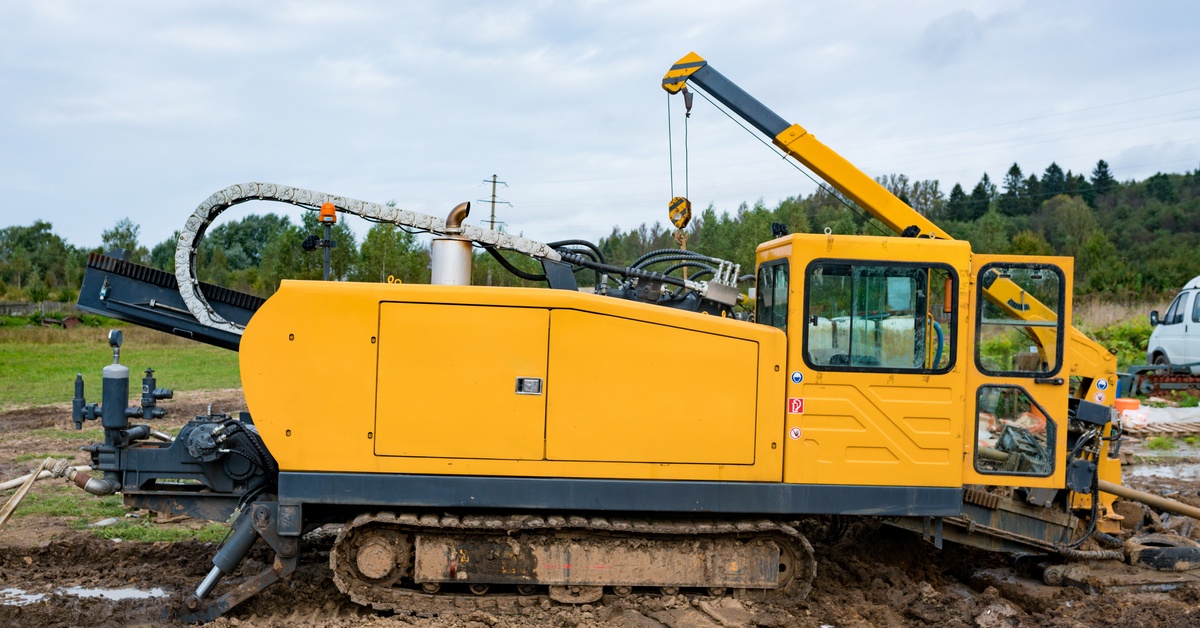 Large yellow directional drilling machine with crawler tracks and a crane operates on a muddy construction site.